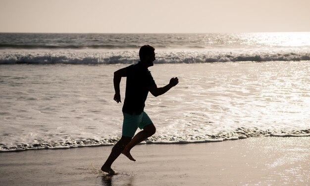 Silhouette of athletic man runner running on summer beach sport