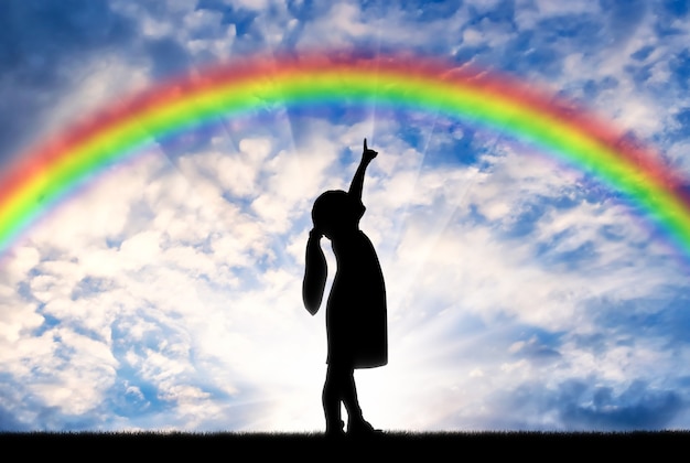 虹の空に指を示す女の赤ちゃんのシルエット。概念的な子供時代のシーン