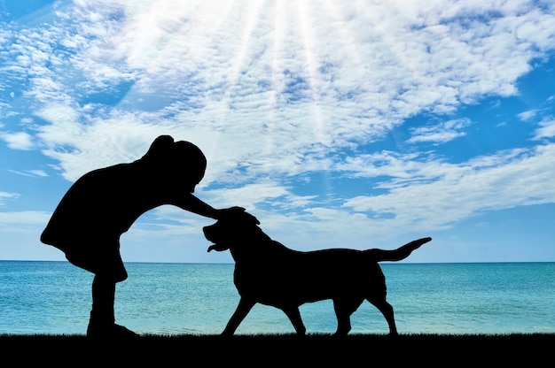 海に対して犬をなでる女の赤ちゃんのシルエット。ペットとの友情の概念