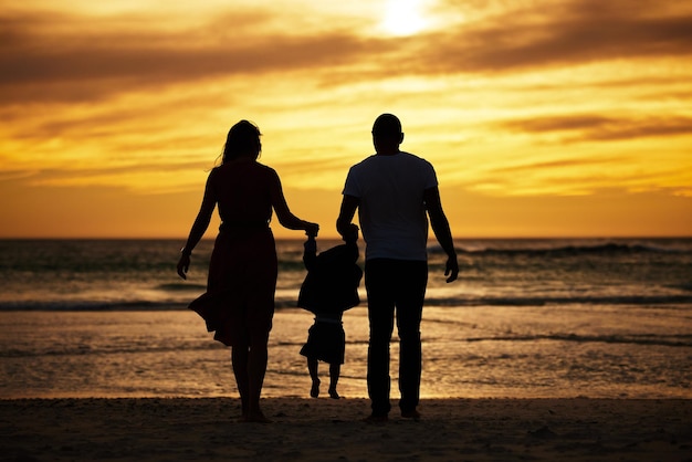 Silhouette beach and family at the sea at sunset holding hands and playing bonding and relax together Shadow happy family and child with parents at sunrise travel freedom and love in Bali