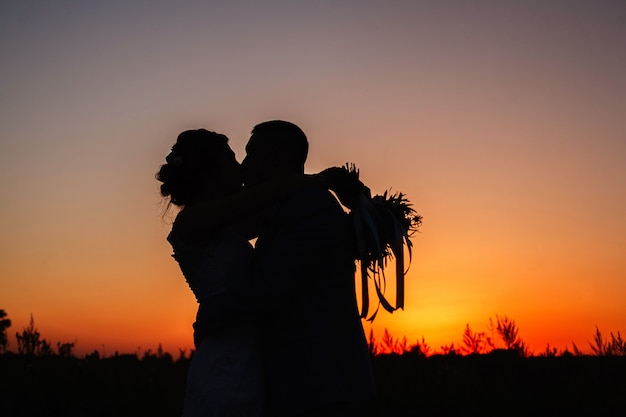 silhouette of  beautiful couple in love hugging outdoors on the sunset. silhouette of bride and groom kissing and hugging outdoors on summer orange sunset. wedding evening. love story concept