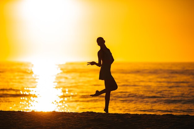 Silhouette of the beautiful girl enjoying beautiful sunset on the beach