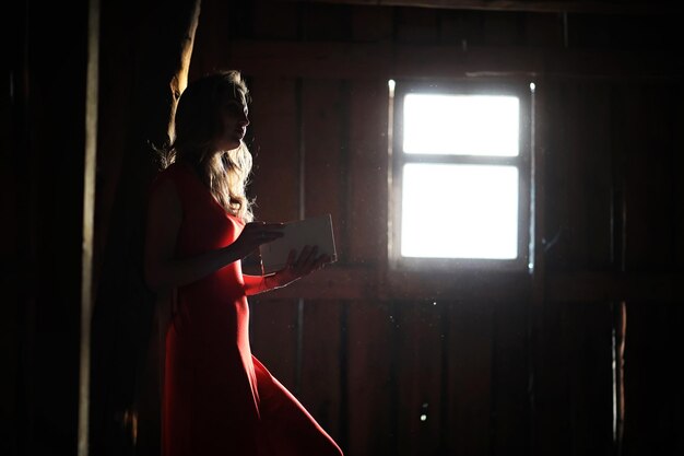 Silhouette of a beautiful girl in a red dress on the background of a window in an old house