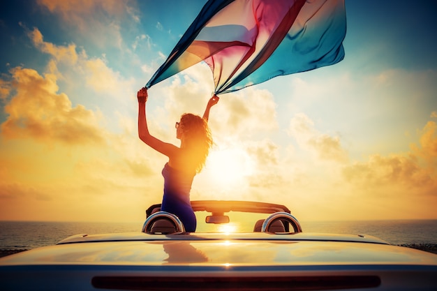 Silhouette of beautiful woman relaxing on the beach Person having fun in cabriolet against blue sky Summer vacation and travel concept