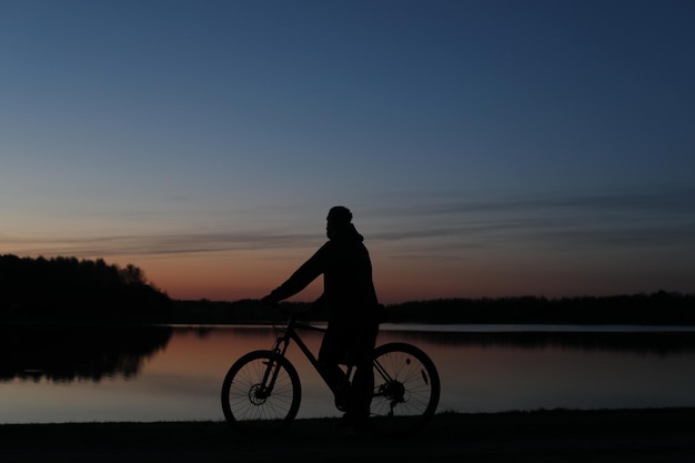 日没時のビーチで自転車に乗る人のシルエット