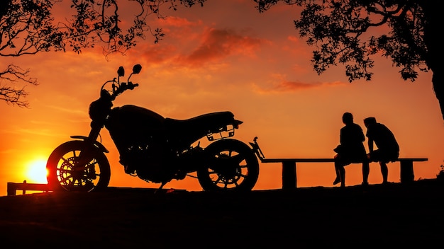 Silhouette big bike motorcycle with couple sitting together on mountain peak at sunset