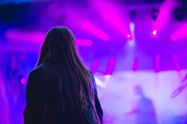 Silhouette of a big crowd at concert against a brightly lit\
stage. night time rock concert with people having fun lifting hands\
up in the air and cheering the musicians