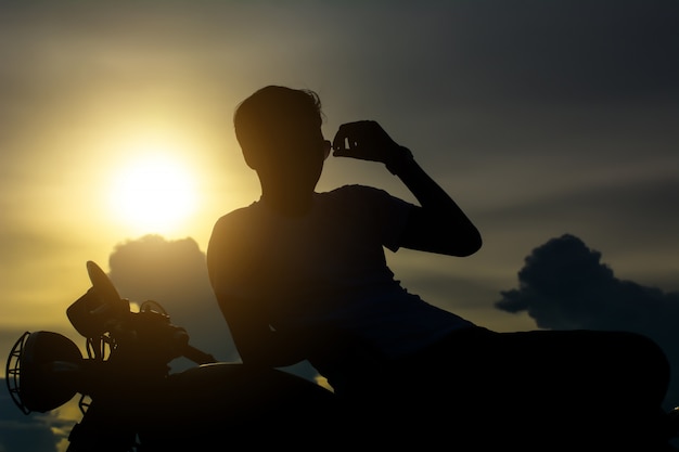 Foto siluetta dell'uomo del motociclista con la sua motocicletta accanto al lago naturale e bello.