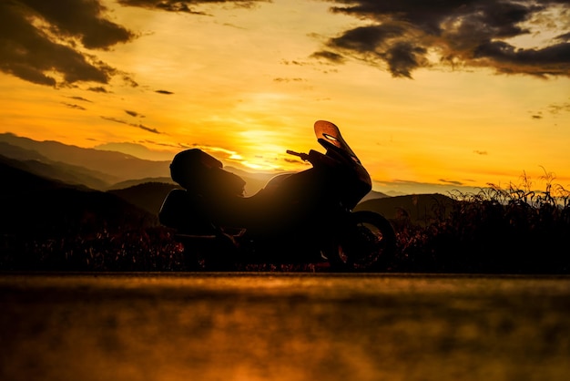 Silhouette of biker with touring motorcycle parking in nature landscape background at sunset