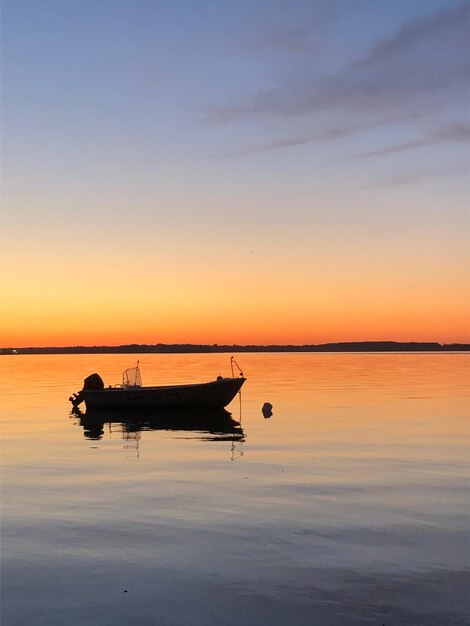 写真 夕暮れの空を背景に海に浮かぶ船のシルエット