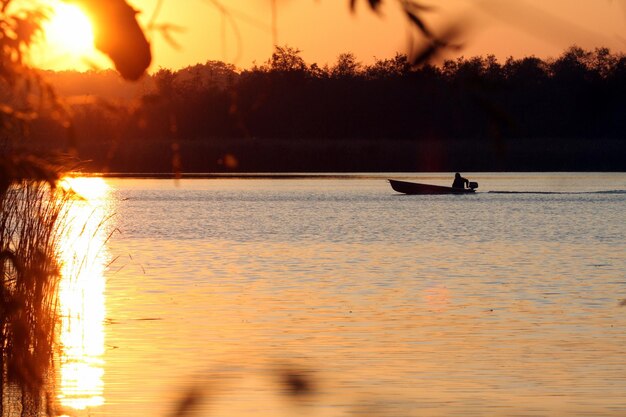 Silhouette boat in lake against orange sky