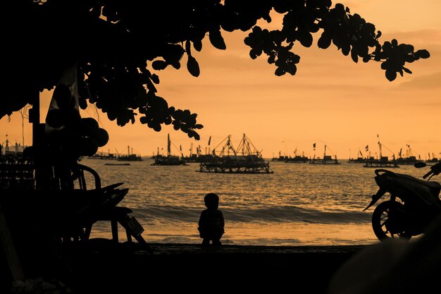 Photo silhouette boy at beach against sky during sunset