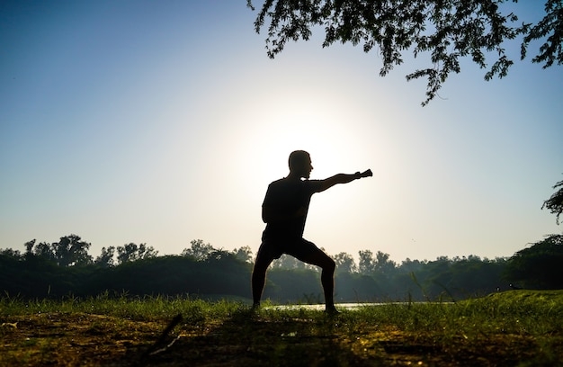 Silhouette di un ragazzo che fa pratica di taekwondo nel parco vicino al sole e al fiume