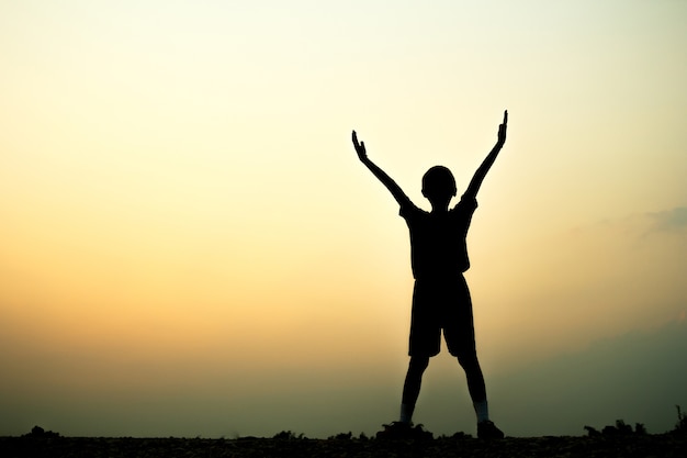 Silhouette of a boy exercising over beautiful sunset background.