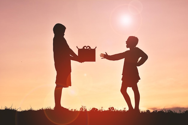 写真 夕暮れの空の向こうのフィールドで少女に贈り物を贈るシルエットの男の子