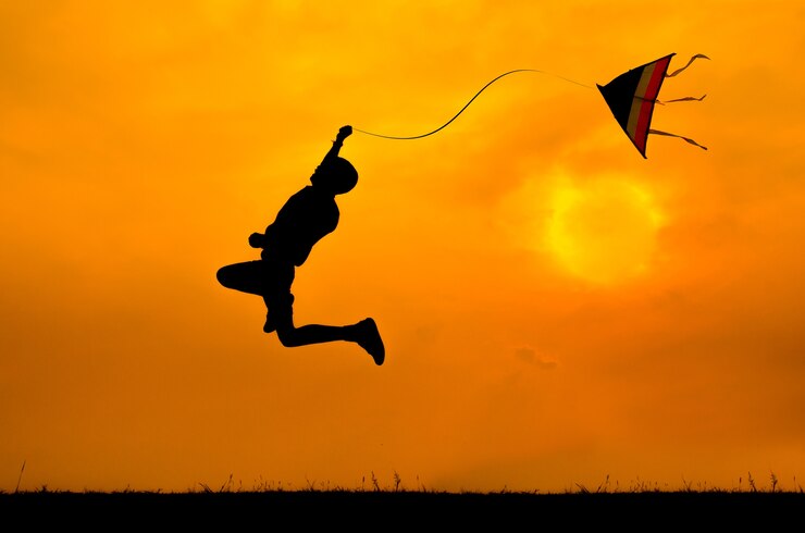 silhouette of A boy jumping with kite to fly