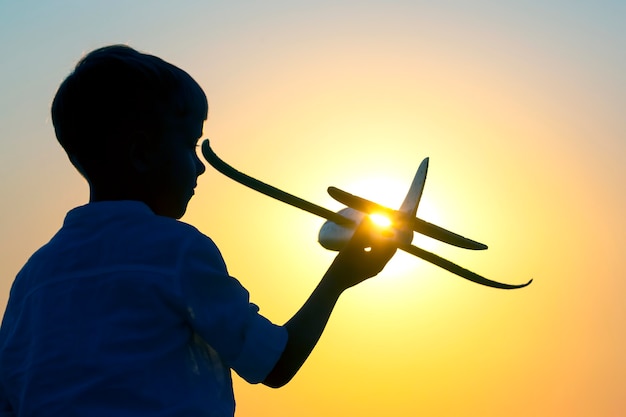 Силуэт мальчика позволяет самолету-модели взлететь в небо на фоне заходящего солнца. Детская мечта будущего летчика