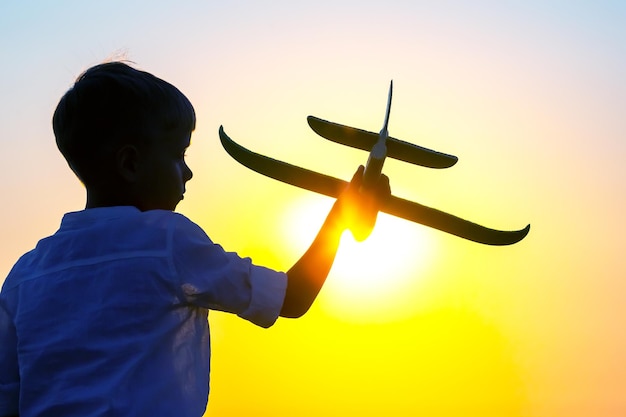夕陽の背景にモデル飛行機が空を飛ぶようにした男の子のシルエット