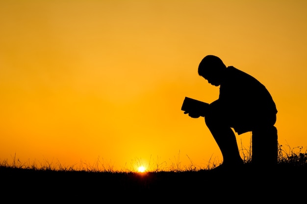 Siluetta del ragazzo che legge un libro durante la priorità bassa di tramonto del cielo