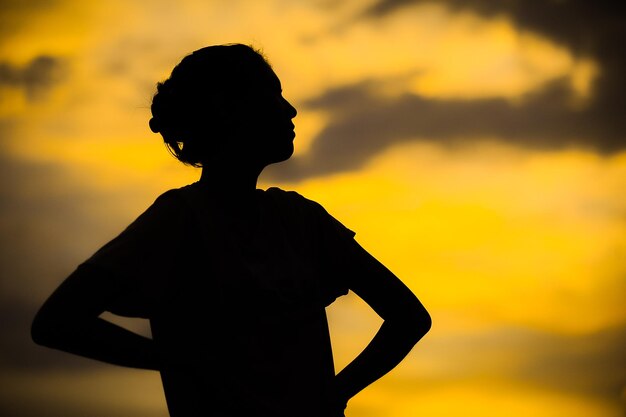 写真 夕暮れの空に向かって立っているシルエットの少年