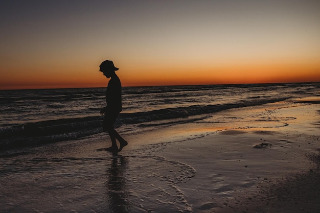 Silhouette boy standing on beach against sky during sunset