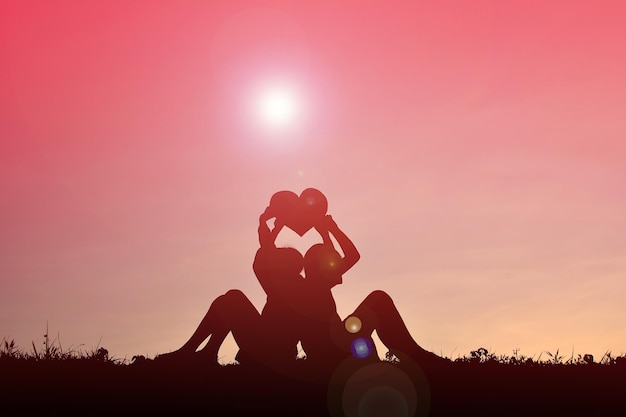 Photo silhouette boys holding heart shape on field against sky during sunset