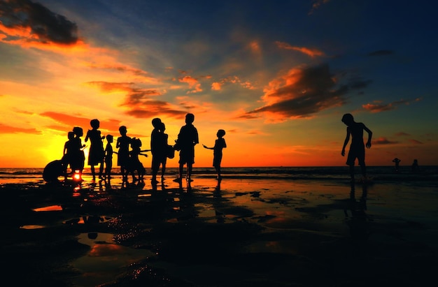 Silhouette boys playing at beach during sunset