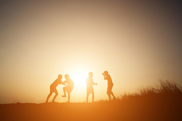 Silhouette boys standing against sky on field during sunset