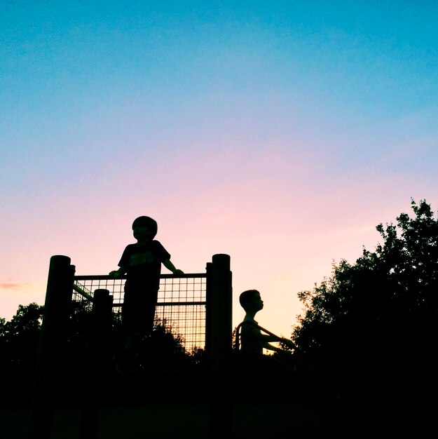 Photo silhouette of boys standing on a climbing frame against sky during sunset