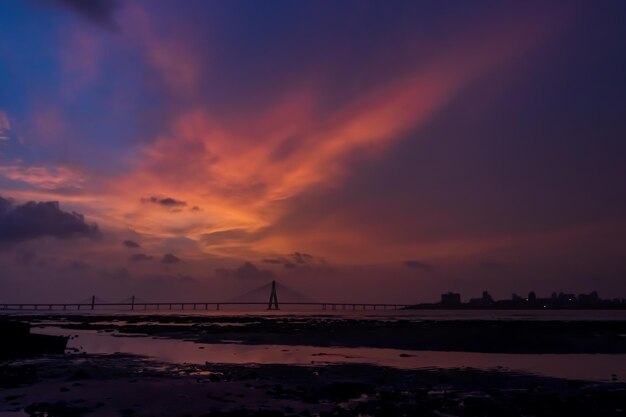 写真 夕暮れの空に照らして海を横切るシルエット橋