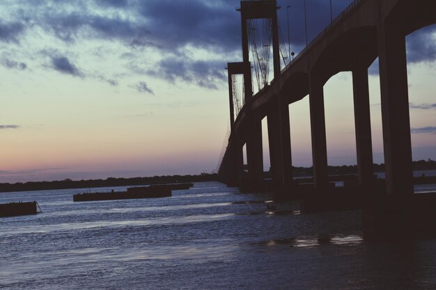 Silhouette of bridge over sea against cloudy sky