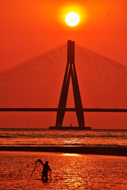 Silhouette bridge over sea against orange sky