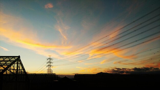 Photo silhouette buildings and electricity pylon against sky during sunset