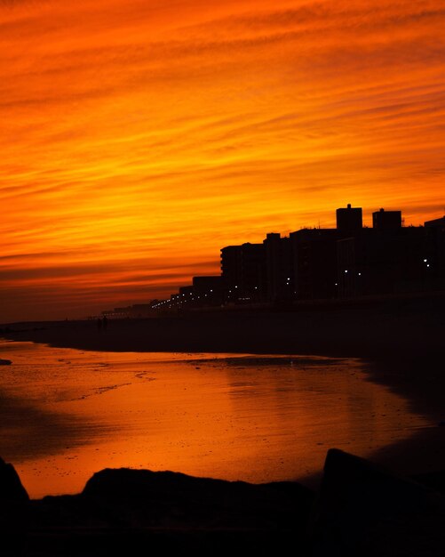 Silhouette buildings at sea shore against sky during sunset