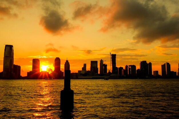 Silhouette buoy in sea against buildings in city during sunset