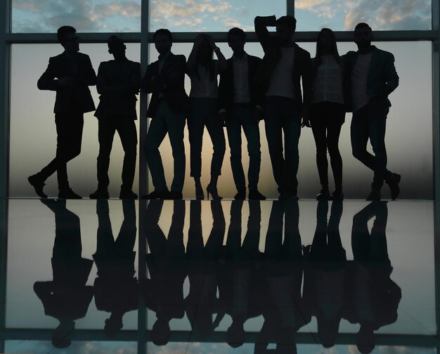 Photo silhouette of a business team standing next to the office window photo with copy space