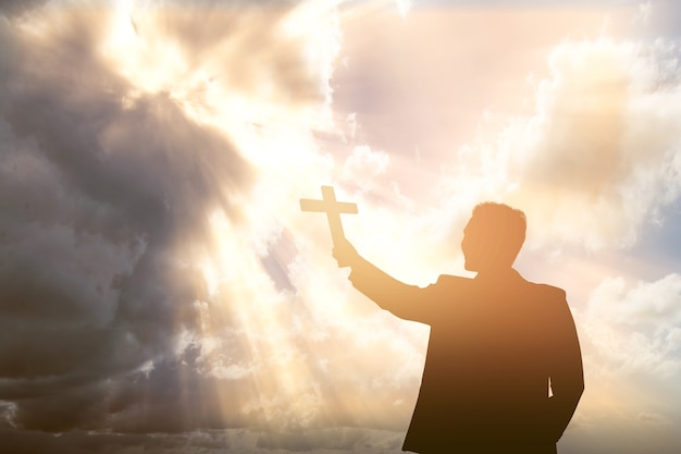 Silhouette of a businessman holding Christian cross with a dramatic sky