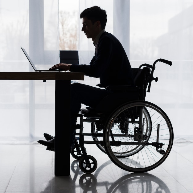silhouette of a businessman sitting on wheelchair using laptop on table
