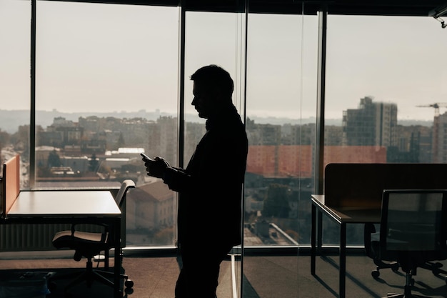 Silhouette of a businessman with phone in his hands standing in\
office