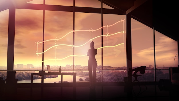 Silhouette of a businesswoman looks at the infographics at sunset