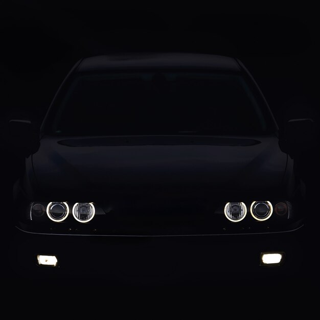 Silhouette of car with headlights on black background.