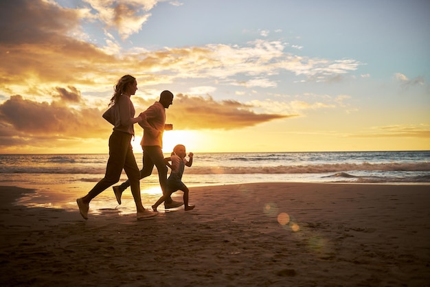 Photo silhouette of a carefree family running and having fun together during sunset on the beach parents spend time with their daughters on holiday little girl playing with her parents while on vacation