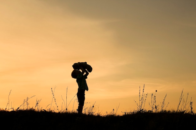 Silhouette of child play with bear on sunset