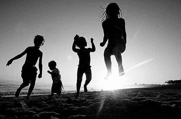 Photo silhouette children on beach against sky during sunset