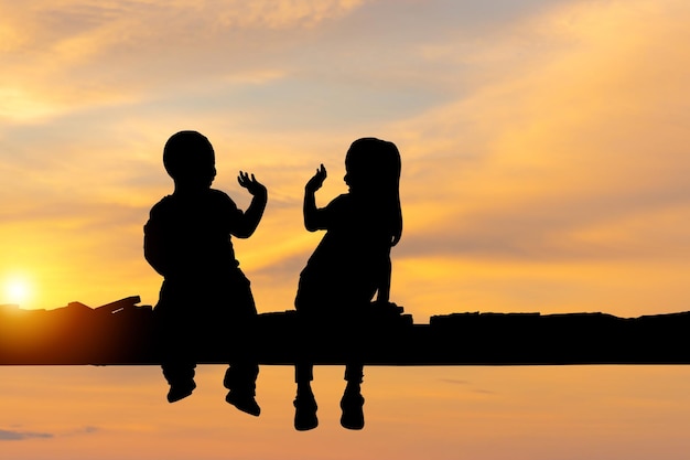 Silhouette of children sitting on the wooden bridge Kids boy and girl reading book outdoor