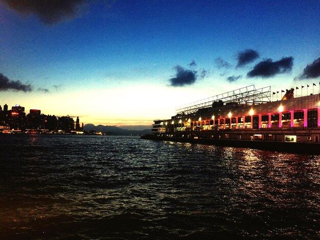 Silhouette city by sea against sky at sunset