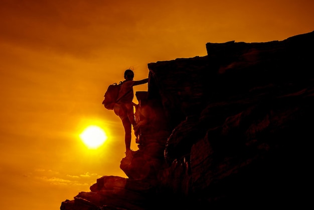 Silhouette climber on the cliff. Sunset and high mountain. Business Success and goal.