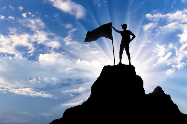 Silhouette of a climber with a flag on top of a mountain. Conceptual scene of success