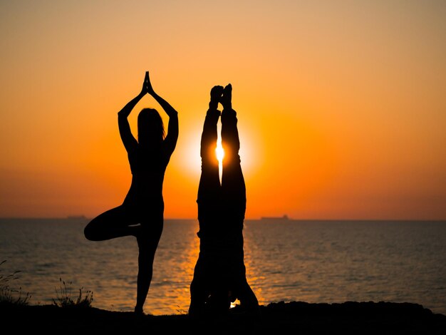 Photo silhouette couple exercising at beach against sky during sunset