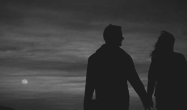 Silhouette couple holding hands against sky at dusk